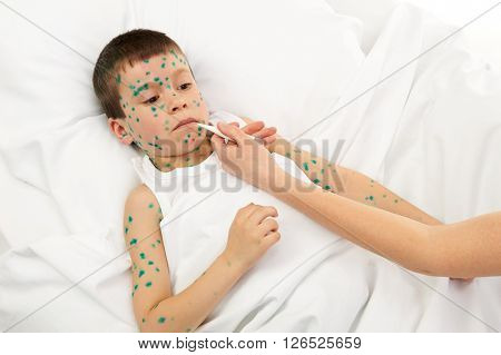 sick child in bed has the virus on skin, mother's hand with thermometer touches the forehead