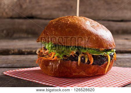 Delicious-looking hamburger on stick. Burger on brown wooden background. Soft buns and quality meat. Dish with unique taste.