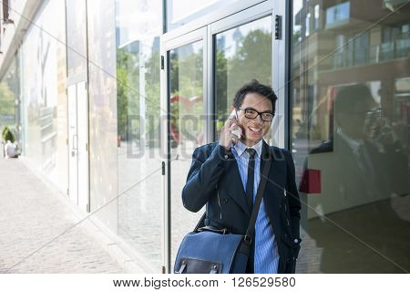 Young asian business man talking on mobile phone outside on city street with copy space