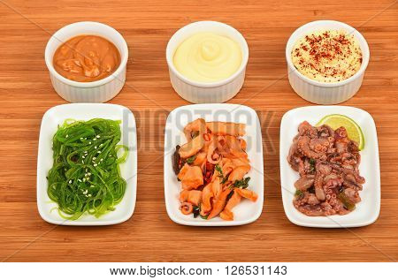 Three portions of seafood marinated salad with octopus cuttlefish squid and seaweeds in white plates with sauce on wooden table high angle view