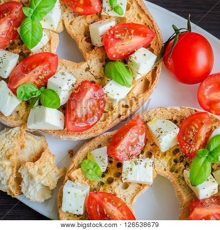 Italian starter friselle. Classical frisella tomato, cheese mozzarella and basil with oregano and olive oil. Dried bread called freselle on white plate. Italian food. Healthy vegetarian food.