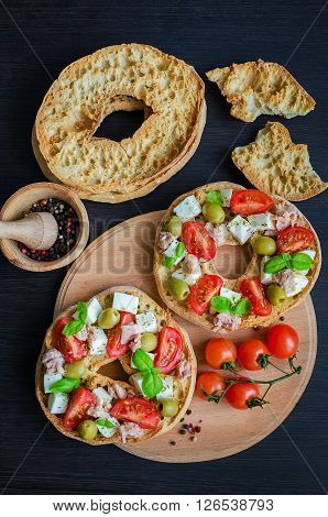 Classical frisella tomato, cheese mozzarella, tuna and olives. Italian starter friselle. Dried bread called freselle on wooden board with tomatoes cherry. Italian food. Healthy vegetarian food.