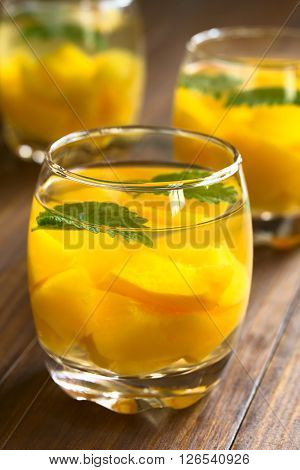 Refreshing peach lemon balm and white wine punch or wine cooler in glasses photographed on dark wood with natural light (Selective Focus Focus on the rim of the glass)