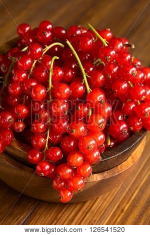 Raw red currants (lat. Ribes rubrum) in wooden bowl photographed on dark wood with natural light (Selective Focus Focus on the red currants in the front)