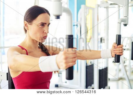 Young pretty Caucasian girl is working out on butterfly machine at the gym