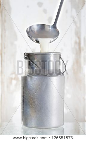 milk pourring from a  adle on a Old milk can , wooden background