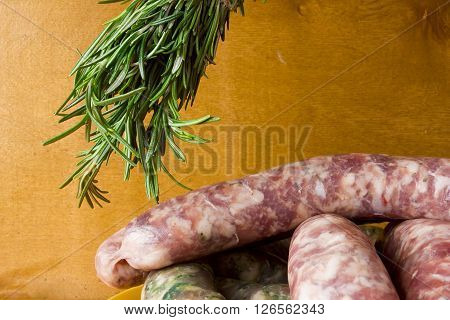 Raw pork sausages and a bunch of rosemary on a wooden background