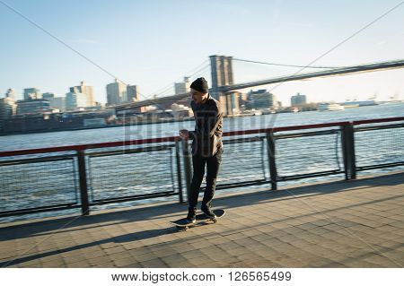 Young skateboarder in casual clothes cruise down on pedestrian walk in New York City.