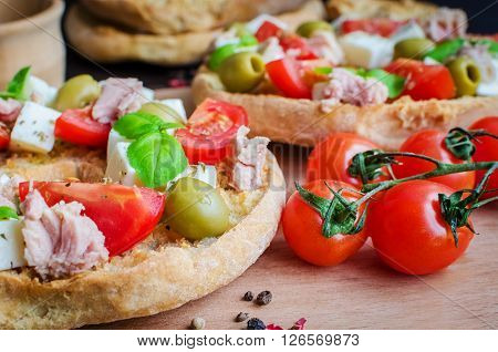 Classical frisella tomato, cheese mozzarella, tuna and olives. Italian starter friselle. Dried bread called freselle on wooden board with tomatoes cherry. Italian food. Healthy vegetarian food.