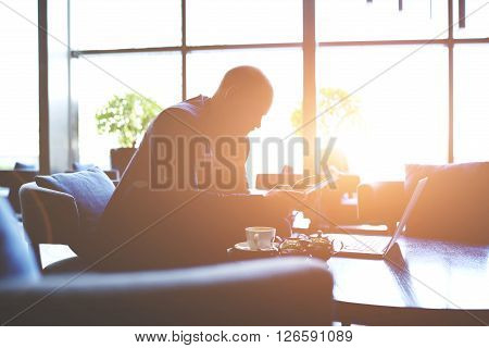 Silhouette of man lawyer is preparing for court hearing while is sitting with net-book and touch pad in office interior. Male managing director is analyzes activity of company by using digital tablet