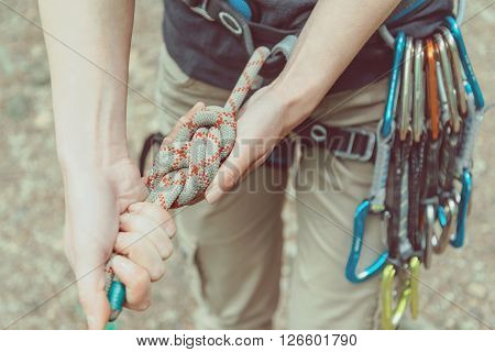 Unrecognizable climber woman wearing in safety harness with quickdraws doing rope eight knot and preparing to climb