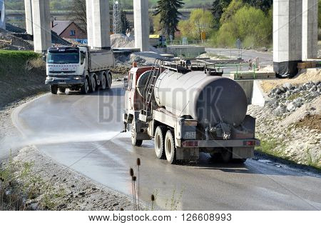 Dolny Hricov Slovakia - April 13 2016: Water tanker splashes water on the road to prevent dust on work site. There is slovak highway labeled 