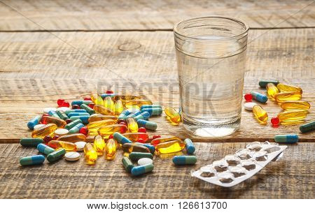 many colorful medical pills and empty pack tablet isolated on wodden table with glass of water