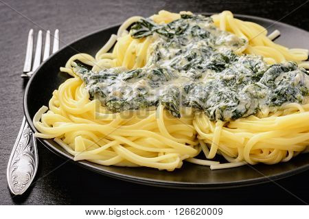 Italian pasta with spinach sauce on black plate.