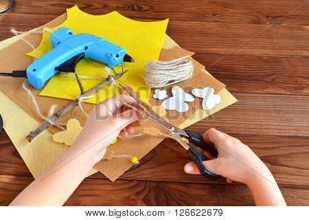 Child holds the scissors and cut out the felt flower. Scissors, hot glue gun, sheets of felt, decorative pendant with felt butterflies and flowers