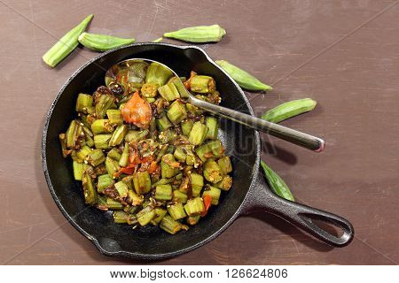Indian Bhindi masala or okra fry in a cast iron pan with copy space on a wooden moosy background.