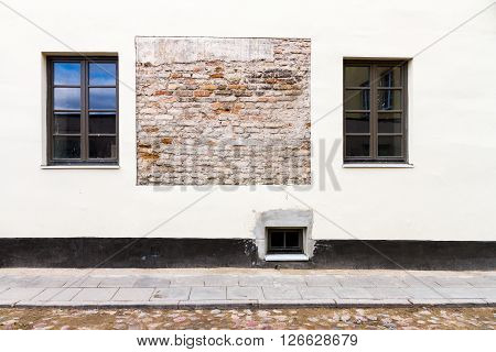 Modern white street wall with some small windows and example of old brickwork