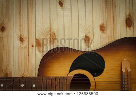 Acoustic guitar resting against a wooden background with copy space