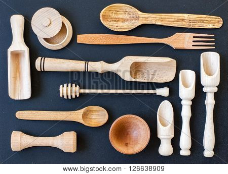 Set of the wooden kitchen utensils on black wooden background. spoon mortar kitchen spatula rolling pin bowl fork. Overhead view of wood utensils on black wood board background.