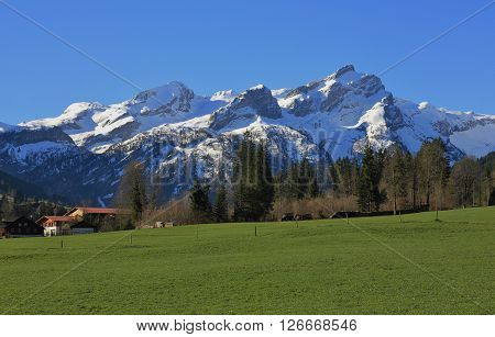 Springtime in the Swiss Alps. Snow capped mountains and green meadow. Spring scene near Gstaad, Bernese Oberland. Nature background.