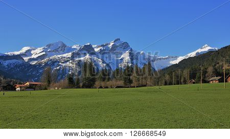 Snow capped mountain range and green meadow. View from Feutersoey, village near Gstaad. Spring scene in the Swiss Alps. Nature background.