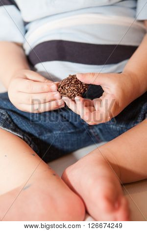 Baby boy eats small chocolate brazilian brigadier candy
