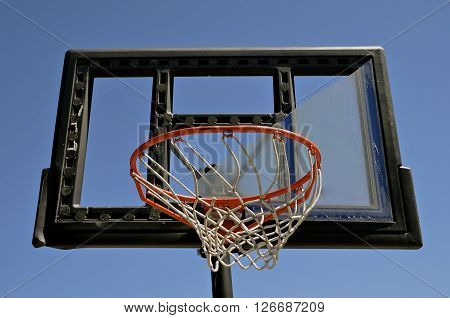 The plexiglass of a backboard is broken on an outdoor basketball court.