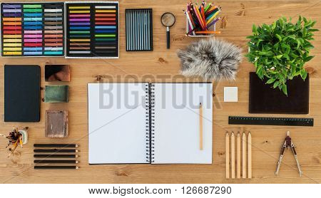 Top view of an artist home studio. Painter worktable in order with a blank sketchpad. Workplace workspace.