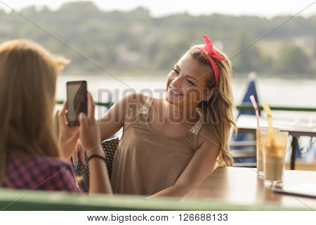 Beautiful young girls sitting in an outdoor cafe drinking coffee and faving fun photographing each other