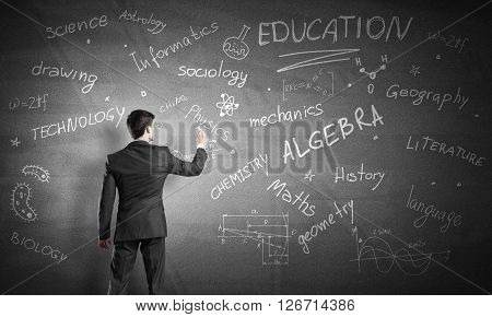 Rear view of man drawing education concept on blackboard with chalk