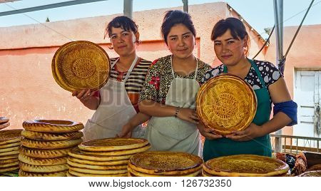 PUNGAN UZBEKISTAN - MAY 6 2015: The young girls - bread sellers poses with the toasted lochira flat breads in rustic food market on May 6 in Pungan.
