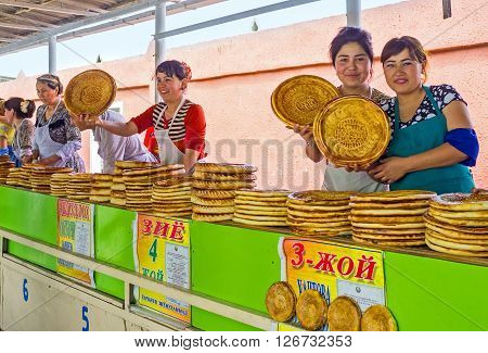 PUNGAN UZBEKISTAN - MAY 6 2015: The young merchants poses with the toasted lochira flat breads in rustic food market on May 6 in Pungan.