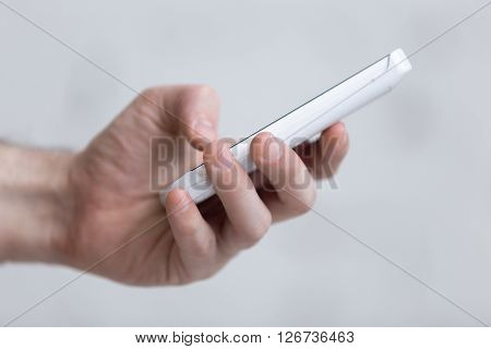 Young man holding white mobile phone in hand. Dialling a number. Using smartphone app. Close-up