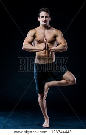 Muscular man balancing on the one leg on dark background