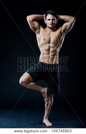 Young strong athlete is making yoga on black background