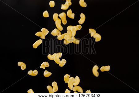 Falling gobetti pasta. Flying yellow raw macaroni over black background. Shallow dof.