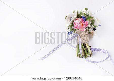 Pastel bouquet from pink tulips violet grape hyacinths white anemones violet veronica and white buttercup with violet ribbon lying on white background