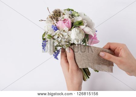 Two hands of the florist are making a beautiful spring bouquet from pink tulips violet grape hyacinths white anemones violet veronica and white buttercups on white background