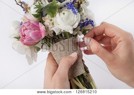 Two hands are making a beautiful spring bouquet from pink tulips violet grape hyacinths white anemones violet veronica and white buttercups using a pin on white background