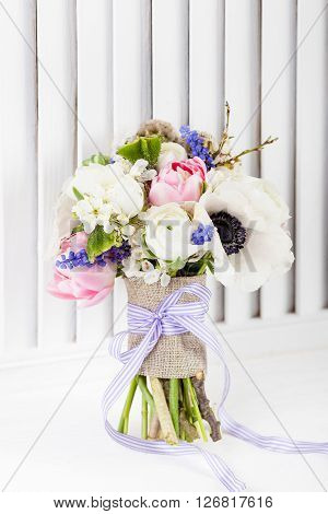 Bouquet from pink tulips violet grape hyacinths white anemones violet veronica and white buttercup with violet ribbon on white wooden stylish shutter background