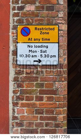 Restricted Zone At Any Time Sign on The Red Brick Wall and No Loading Times