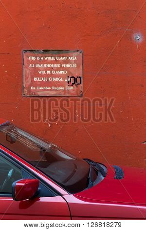 Sign on red wall - This is a Wheel Clamp Area All Unauthorised Vehicles Will be Clamped Release Charge 30 100 Pounds The Clarendon Shopping Centre