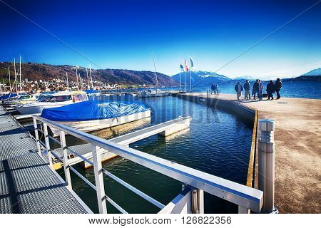 ZUG SWITZERLAND - March 26 2016 - People walking along the embankment in the center of city Zug with the Rigi mountain and Zugersee in the background.
