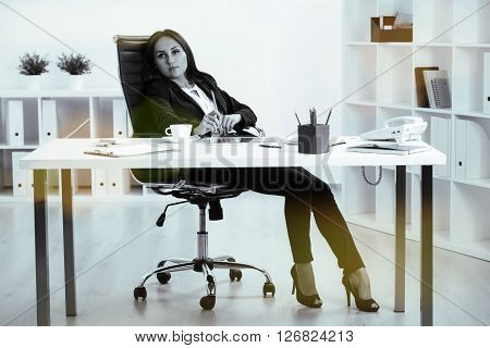 Black and white pictue of tired businesswoman sitting in swivel chair at office desk