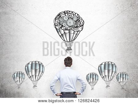 Businessperson looking at airballoons and gears sketch on concrete wall
