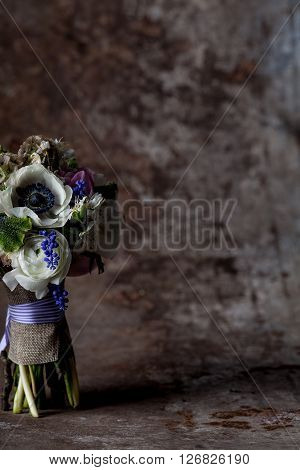 Bouquet from pink tulips violet grape hyacinths white anemones violet veronica and white buttercup with violet ribbon standing on rought metal background with rust
