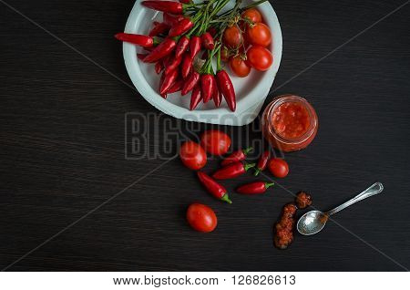 Adjika fresh grated red pepper and chili. Glass jar of homemade tomato sauce with fresh ingredients on dark wooden background. Red hot chilli pepper and ingridients for sause. Top view. Copy space.