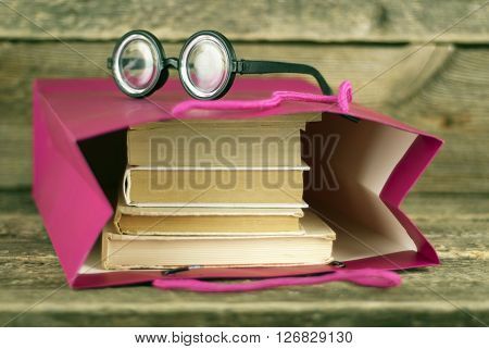 Paper bag with books on a wooden background and glasses shallow dof