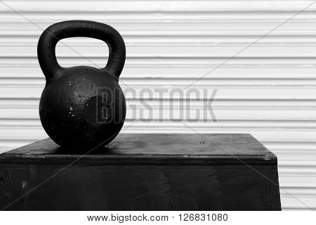 Black kettle bell on a black jump box, against a white roll-up door