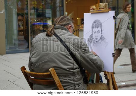 Frankfurt am Main, Hessen, Germany - April 18, 2016: A street artist drawing a picture of a boy. He makes a living by drawing people's face on the street.